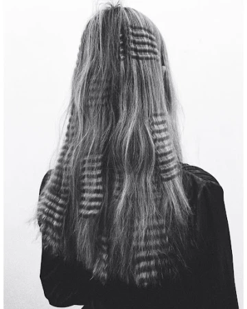 Back view of a woman with long, gray, wavy hair styled with patterned hair clips, set against a plain white studio backdrop.