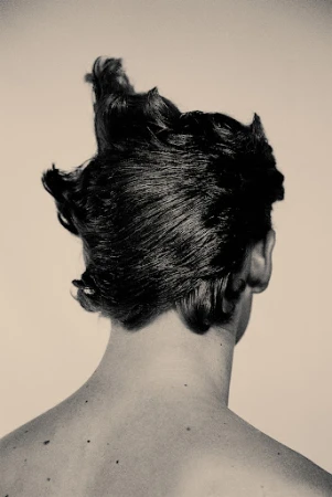 Back of a person's head with dark styled hair and bare shoulders against a neutral light background by Quentin Guyen