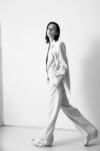 Monochrome portrait of a woman walking in an off-white linen suit against a bright white backdrop, capturing a minimalist aesthetic.