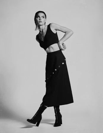 Model with slicked-back hair wearing a black crop top and long skirt against a plain white background