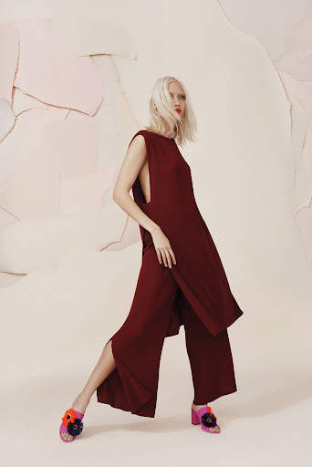 Fashion editorial shot of a woman with white hair wearing a maroon two-piece outfit with flower embellished heels in a studio setting.