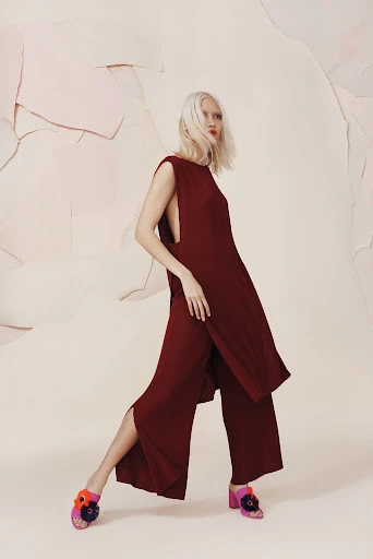Fashion editorial shot of a woman with white hair wearing a maroon two-piece outfit with flower embellished heels in a studio setting.