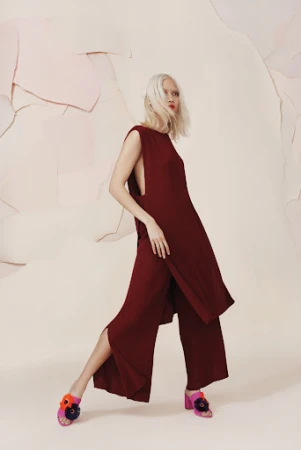 Fashion editorial shot of a woman with white hair wearing a maroon two-piece outfit with flower embellished heels in a studio setting.