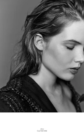 Monochrome portrait of a woman with wet look hair and textured dark clothing against a grey background.