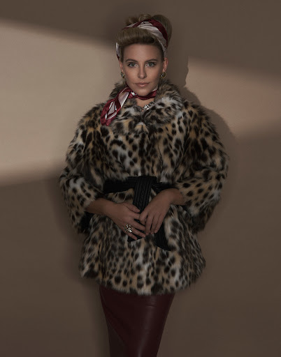 Adult woman poses in a vintage-inspired, leopard-print coat with a red pencil skirt against a neutral background with lighting effects.