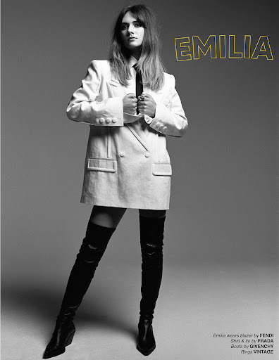 Monochrome portrait of a woman in an oversized white blazer and black thigh-high boots against a plain grey background