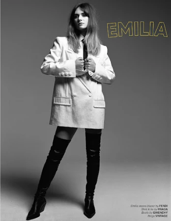 Monochrome portrait of a woman in an oversized white blazer and black thigh-high boots against a plain grey background