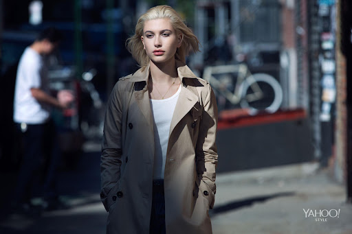 Blonde woman wearing a tan trench coat walking down an urban street