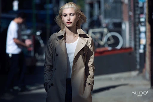 Blonde woman wearing a tan trench coat walking down an urban street