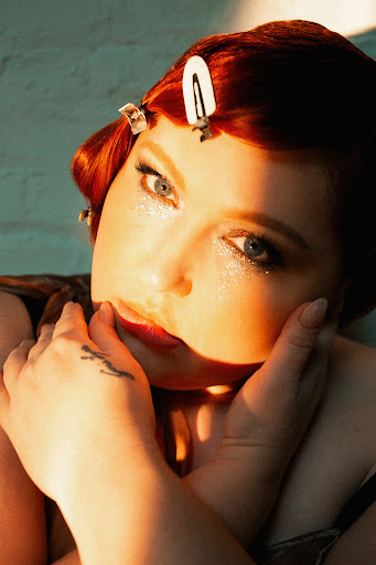 Close-up of an adult woman with auburn hair styled in waves and accessorized with hair clips. She is fair-skinned with red lipstick.