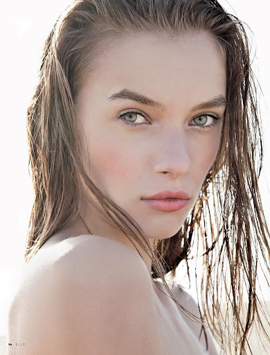 Close-up portrait of a woman with wet, slicked-back brown hair and natural makeup against a bright outdoor background