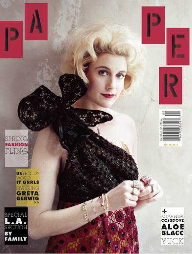Fashion magazine cover featuring a woman with blonde hair wearing an off-the-shoulder dress with a large black bow accent.
