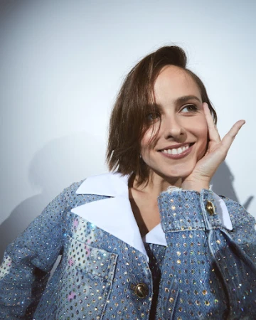 Close-up portrait of a smiling woman wearing a rhinestone-embellished denim jacket with a white collar.