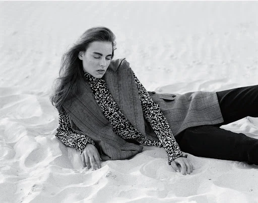 Model lying on sandy dunes wearing a patterned turtleneck top and sleeveless blazer with hair styled by Seiji