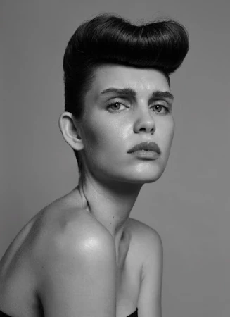 Portrait of a woman with sculptural styled dark hair and a neutral expression against a plain grey background