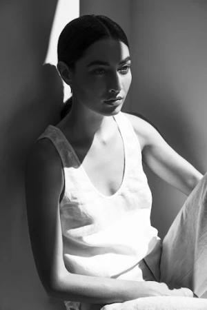 Monochrome portrait of a woman in a white tank top with stark shadows crossing her face.