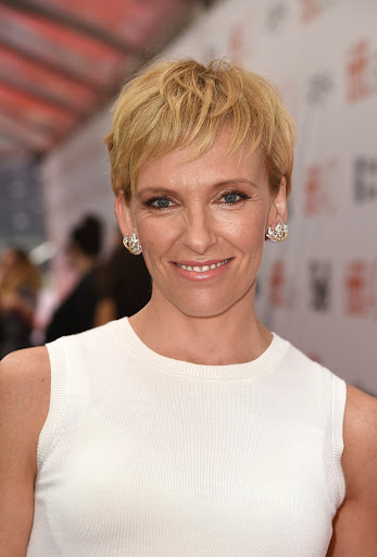 Close-up shot of Toni Collette with short blonde hair, smiling in a sleeveless white top at a red carpet event.