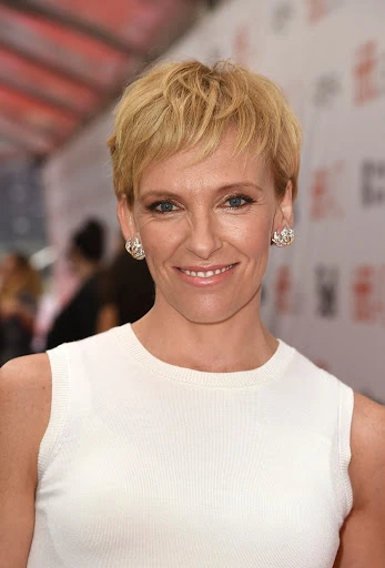 Close-up shot of Toni Collette with short blonde hair, smiling in a sleeveless white top at a red carpet event.