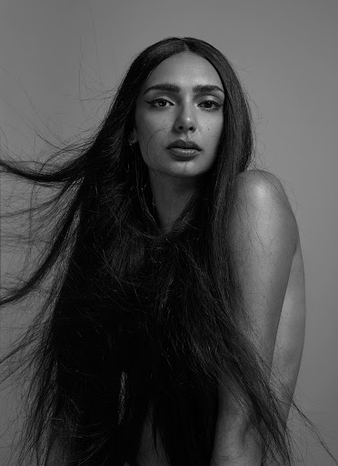 Striking black and white portrait of a woman with long, flowing dark hair against a neutral backdrop in a photo studio setting.