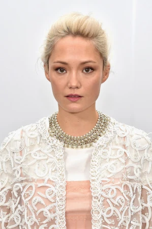 Portrait of a woman with blonde hair wearing a white embroidered jacket and heavy pearl statement necklace