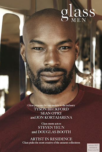 Glass Men magazine cover featuring a headshot of a bald Black male model in a maroon shirt, looking directly at the viewer. 