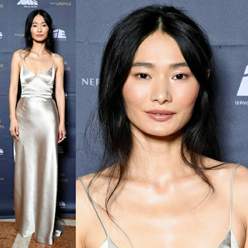 Asian woman in silver gown at event. Portrait of elegant woman with long black hair in formal attire at indoor venue backdrop.