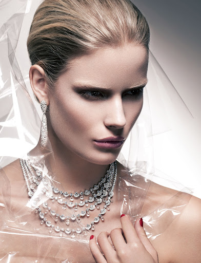 Blonde woman with a multi-layered diamond necklace, wearing matching earrings, with dramatic makeup and clear plastic draped around her neck.