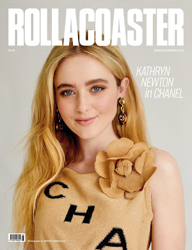 Kathryn Newton on the cover of ROLLACOASTER magazine, wearing a neutral-toned top with black lettering and a tan floral embellishment.