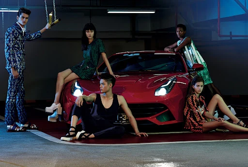Fashion editorial shot in a parking garage featuring a red sports car surrounded by five fashion models wearing patterned outfits.