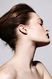 Profile portrait of a woman with dark red lips, styled hair, and freckles against a neutral background.