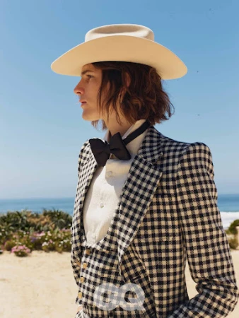 Profile portrait of a person wearing a beige cowboy hat, black bow tie, and black and white gingham suit jacket by the coast.