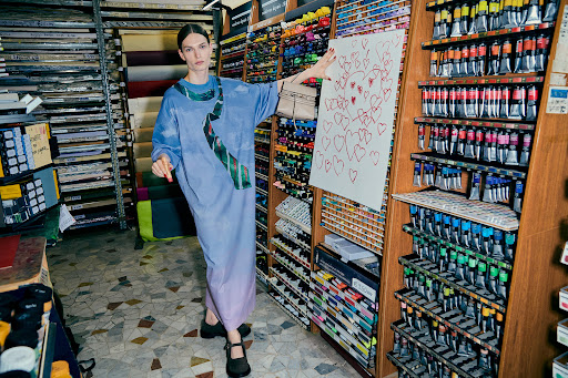 Model wearing a blue ombre dress holding up a large paper with red heart drawings in an art supply store.
