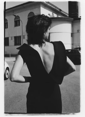 Black and white portrait of a woman seen from behind wearing a black backless dress outdoors in a street setting