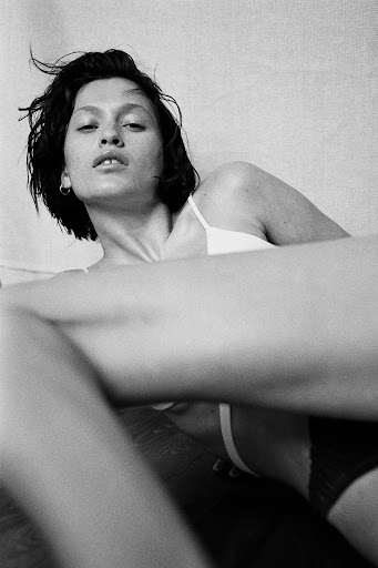 Monochrome portrait of a young adult woman in a bralette lying down with a relaxed facial expression and an arm in the foreground.