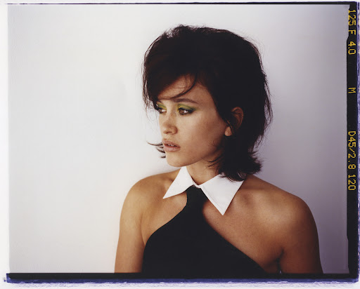 Side profile portrait of a woman with dark hair, wearing a black dress with a white collar, against a plain white background. 