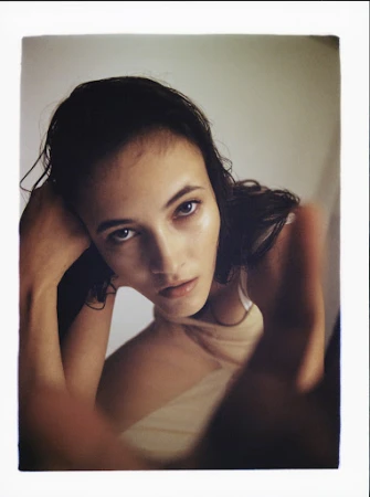 Close up portrait of a young woman with dark wet hair looking directly at camera against a neutral background