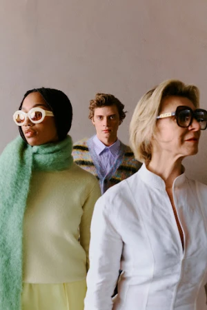 Three models with sunglasses and varied knitwear and shirts posed against a neutral wall