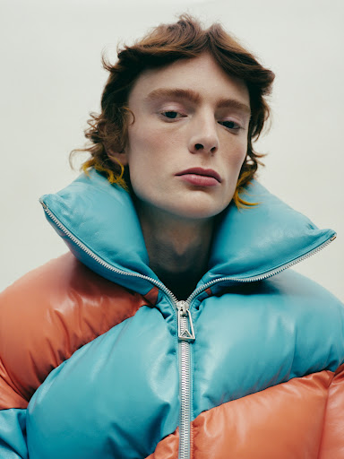 Close-up studio portrait of a male model in a color-blocked puffer jacket, featuring a high collar, and a silver zipper.