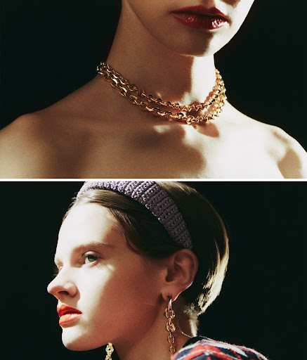 Close-up shot of a woman with gold chain jewelry and a lilac headband against a dark background, fashion and beauty focused.