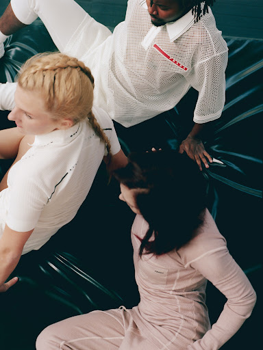 Three fashion models in coordinated athletic-inspired clothing on a black surface, showcasing modern design and style in a studio setting.