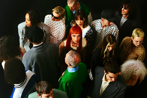 High-angle group portrait of diverse fashion models with varied hairstyles against a dark background, styled by Simone Prusso.