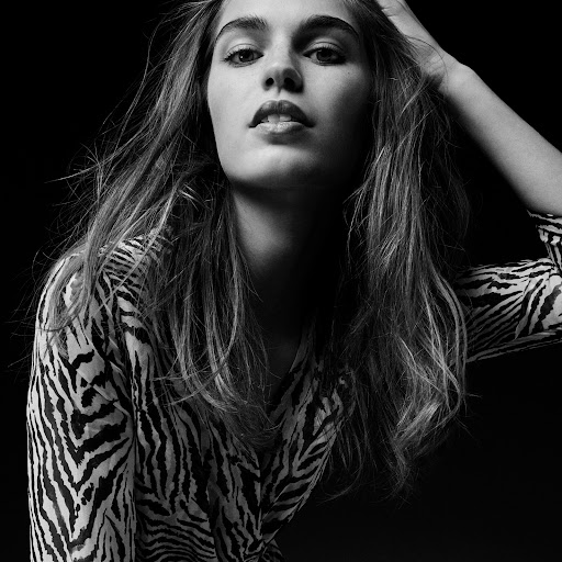 Black and white portrait of a woman with long hair in a zebra print shirt posing against a dark background.