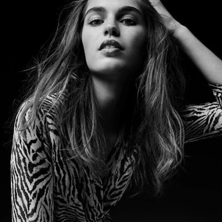 Black and white portrait of a woman with long hair in a zebra print shirt posing against a dark background.