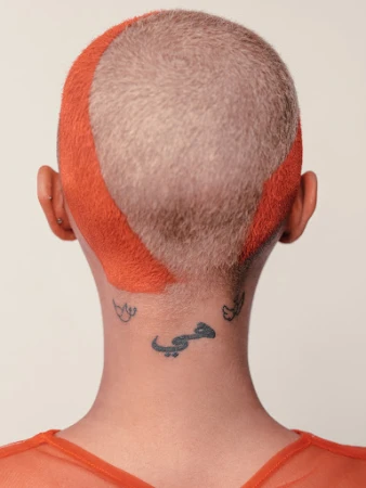 Back of a person's head with an orange-dyed buzz cut and multiple tattoos on the neck. Focus on personal style and body art.