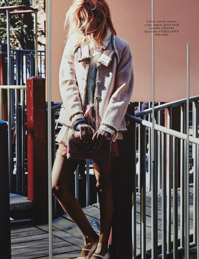 Fashion model poses on playground wearing pink tweed jacket, pale blue top, pink shorts and Mary Jane shoes with a matching shoulder bag.