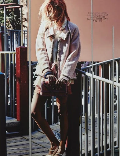 Fashion model poses on playground wearing pink tweed jacket, pale blue top, pink shorts and Mary Jane shoes with a matching shoulder bag.