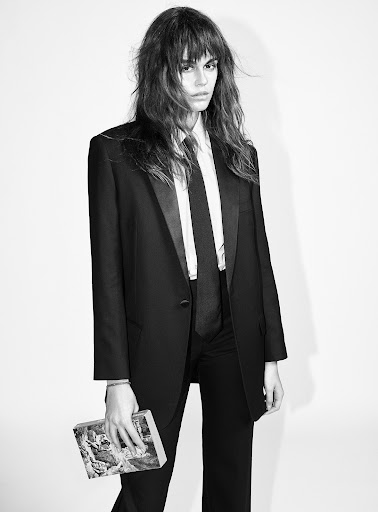 A solitary figure in black and white, a woman in a suit and tie holds a book in a photo studio, creating a timeless, classic portrait.