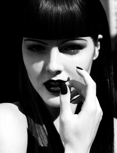 Striking black and white portrait of a woman with dark lipstick, dark fingernails and a blunt fringe hairstyle, looking at the camera.