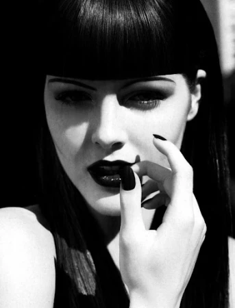 Striking black and white portrait of a woman with dark lipstick, dark fingernails and a blunt fringe hairstyle, looking at the camera.