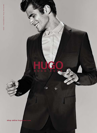 Man in a suit smiles in a fashion shot for Hugo Boss, showcasing a black double-breasted suit and a white button-down shirt.